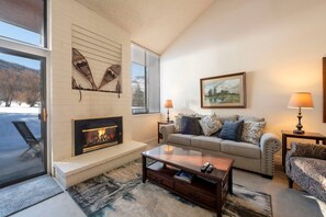 A living room with a fireplace, a sofa set, a coffee table, and a painting on the wall. - Park Ave 251 | Heated Pool | Hot Tub | Vaulted Ceilings | Fireplace | Laundry | Near PCMR (Park City)