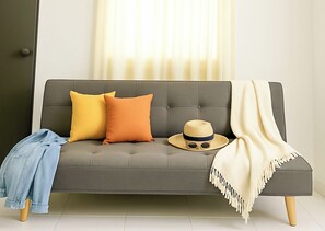 Ein graues Sofa mit zwei Kissen, einem Hut und einer Decke.