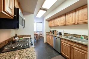 A kitchen with a stove, microwave, and dishwasher, wooden cabinets, granite countertops, and a window with blinds. - Park Ave 292 | Heated Pool | Hot Tub | Fireplace | Laundry | Trail-Side | Near PCMR | Free Bus (Park City)