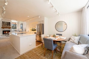 A modern kitchen with a central island, dining area with a round table, and a living room with a sofa and a fireplace. - Park Ave 299 | Heated Pool | Hot Tub | Remodeled End Unit | Fire Table Atrium | Patio & Grill (Park City)