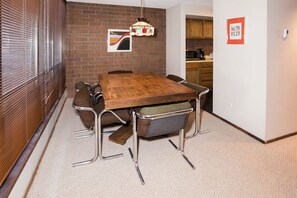 A dining area with a wooden table, metal chairs, a hanging light fixture, and a brick wall. - Park Ave 314 | Heated Pool | Hot Tub | Fireplace | Laundry | Trail-Side | Near PCMR (Park City)