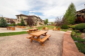 A patio area with picnic tables and chairs, surrounded by a landscaped garden and residential buildings. - Bear Hollow 4402 | Pool & Hot Tubs | Top Floor | Mtn View Balcony | Fireplace | Near Outlets (Park City)