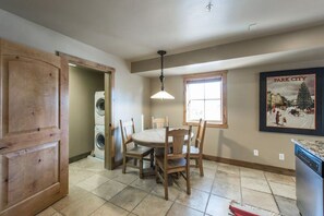 A dining area with a round table and chairs, a washing machine, a ceiling light, and a framed picture on the wall. - Jupiter Inn 10 | Community Hot Tub | Gas Fireplace | A/C | Laundry | Walk to Dining | Free Bus (Park City)