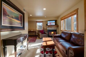 A living room with a fireplace, a television, a sofa, and a coffee table. - Jupiter Inn 10 | Community Hot Tub | Gas Fireplace | A/C | Laundry | Walk to Dining | Free Bus (Park City)