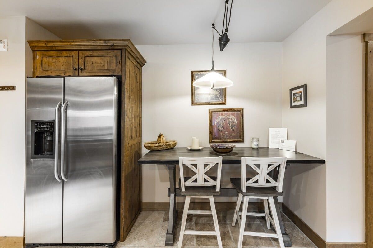 A kitchen with a stainless steel refrigerator, wooden cabinets, a bar stool, and a pendant light.