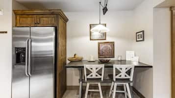 A kitchen with a stainless steel refrigerator, wooden cabinets, a bar stool, and a pendant light.