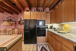 Eine kleine Küche mit Holzschränken, einem schwarzen Kühlschrank, einer Mikrowelle und einem Herd.