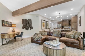 A modern living room with a leather sectional sofa, a round coffee table, and a dining area with a wooden table and chairs. - Powder Run C13 | Private Hot Tub | 1 Block to Snow Park | Slope Views | Remodeled | Heated Floors (Park City)