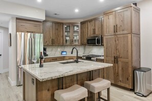 Cozinha com armários de madeira, geladeira de aço inoxidável, micro-ondas e bancada de mármore.
