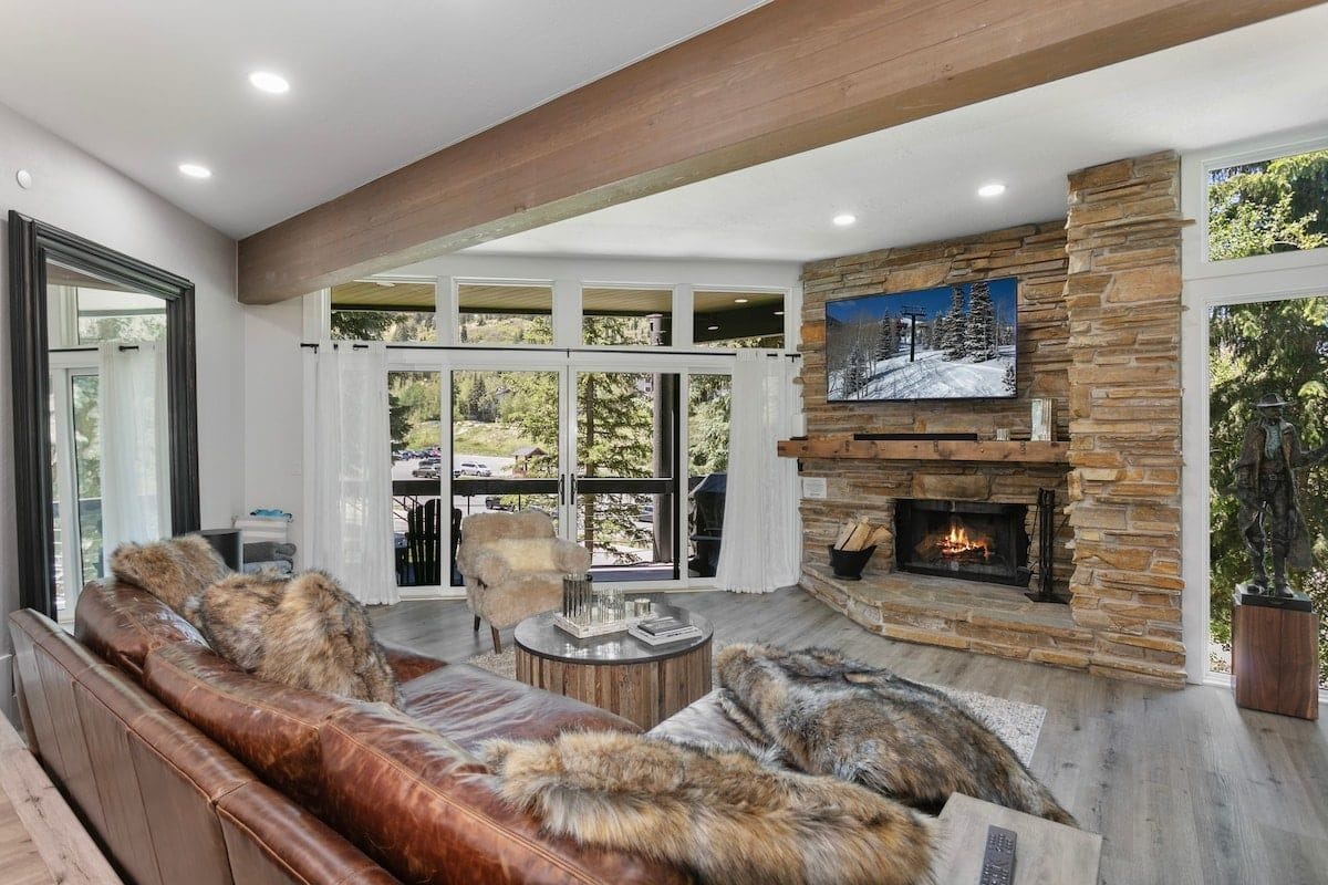 A modern living room with a stone fireplace, leather sofa, and a large window overlooking a scenic outdoor area.