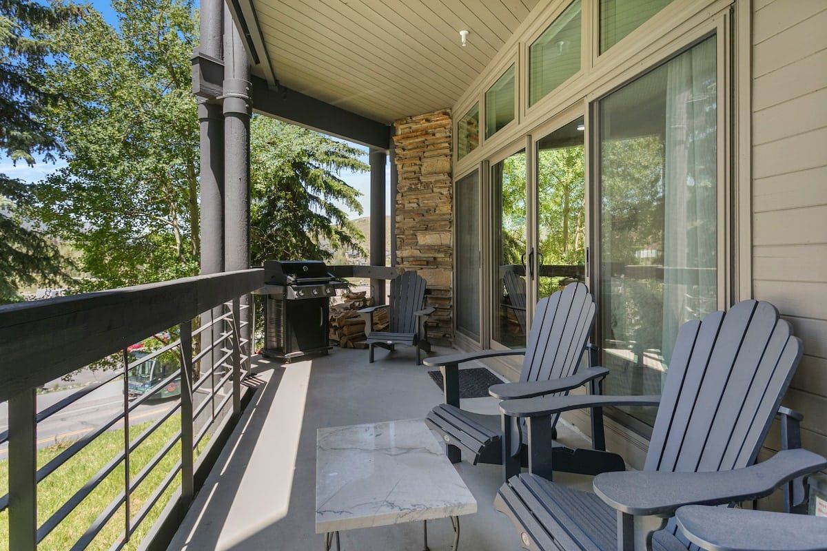 Un espace extérieur abrité, équipé de fauteuils Adirondack, d’un barbecue et d’un pilier en pierre.