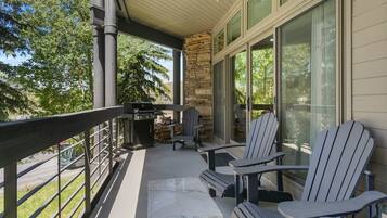 A covered outdoor area with Adirondack chairs, a grill, and a stone pillar.