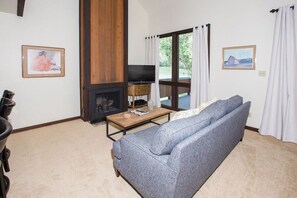 A living room with a sofa, a television, a fireplace, and a view through a glass door. - Three Kings 37 | Walk to Three Kings Lift | Heated Pool | Hot Tub | Sauna | Garage Parking (Park City)
