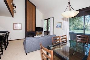 A modern living room with a glass dining table, wooden chairs, a grey sofa, a fireplace, and a television. - Three Kings 37 | Walk to Three Kings Lift | Heated Pool | Hot Tub | Sauna | Garage Parking (Park City)