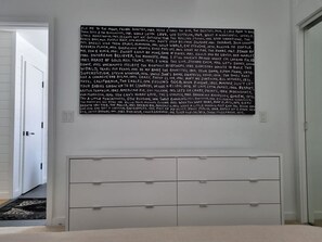 Une pièce avec une grande affiche noir et blanc au mur, une commode blanche avec des tiroirs et une porte donnant sur une autre pièce.
