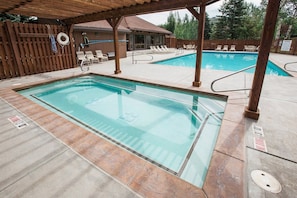 A rectangular pool with a wooden deck surrounding it, a covered seating area with chairs, and a wooden fence in the background. - Three Kings 80 | Walk to Three Kings Lift | Heated Pool | Hot Tub | Remodeled | Original Artwork (Park City)