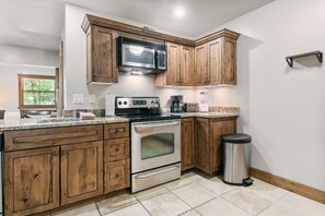 A kitchen with wooden cabinets, a stainless steel oven, a microwave, and a trash can. - Jupiter Inn 11 | Community Hot Tub | Stone Fireplace | A/C | Laundry | Near Golf Course | Free Bus (Park City)