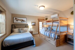 Ein Schlafzimmer mit einem Einzelbett, einem Etagenbett, einem Nachttisch, einer Lampe, einem gerahmten Bild und einer Deckenleuchte.