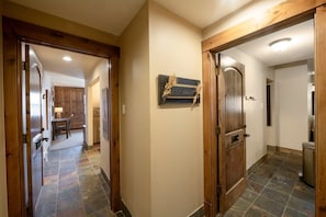 Um corredor com portas de madeira, uma placa na parede e uma área de cozinha ao fundo.