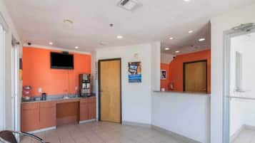 A hotel lobby with a reception desk, a television mounted on the wall, and a door leading to the kitchen area.