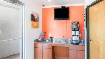 A small kitchenette with a coffee machine, a television mounted on the wall, and a door labeled 'Cups'.
