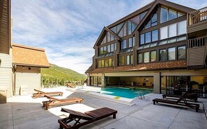 A two-story building with a swimming pool, outdoor seating, and a view of a mountainous landscape. - Resort Center 5013 | Ski-In/Ski-Out | Pool & Hot Tub Access | Fireplace | 3 Baths | Sleeps 8 (Park City)