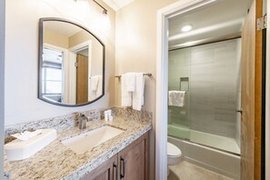 Une salle de bain avec un lavabo sur un plan de travail en granit, un miroir, une cabine de douche en verre et des toilettes.