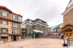 Un immeuble à plusieurs étages dont le rez-de-chaussée est occupé par des commerces, notamment un magasin de location de matériel de ski et un restaurant.
