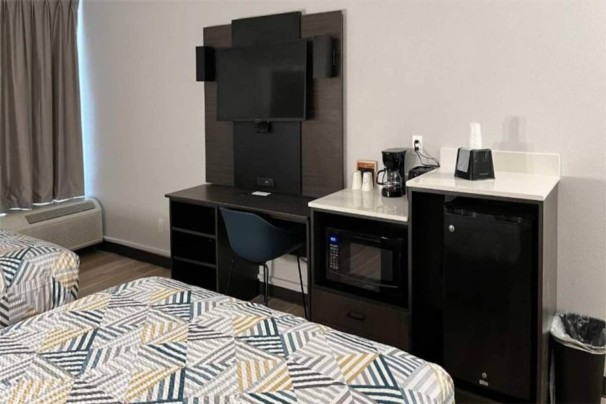 A hotel room with a bed, a desk, a chair, a television, a coffee maker, and a trash bin.