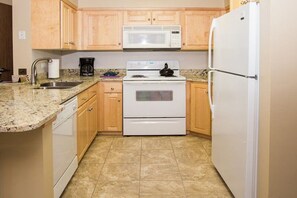 A kitchen with wooden cabinets, a white stove, a microwave, and a refrigerator. - Resort Center 5040 | Ski-In/Ski-Out | Pool & Hot Tub Access | Fireplace | Steps to Lifts (Park City)