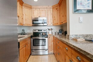 A kitchen with wooden cabinets, a stainless steel oven, and a microwave. - Resort Center 5064 | Ski-In/Ski-Out | Pool & Hot Tub Access | Renovated | Fireplace | Laundry (Park City)