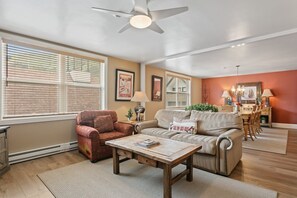 A living room with a ceiling fan, a sofa, a coffee table, and a dining area with chairs and a table. - Resort Center 5064 | Ski-In/Ski-Out | Pool & Hot Tub Access | Renovated | Fireplace | Laundry (Park City)