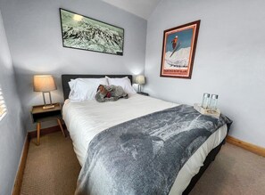 A bedroom with a bed, a nightstand, a lamp, a blanket, a poster, and a small table with items. - Fox Pointe A2 | Redstone Village | Walk to Shops & Dining | Garage | Fireplace | Patio & Grill | A/C (Park City)