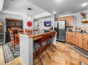 A modern kitchen with a central island, wooden cabinets, a stainless steel refrigerator, and a dining area with chairs. - Fox Pointe A2 | Redstone Village | Walk to Shops & Dining | Garage | Fireplace | Patio & Grill | A/C (Park City)