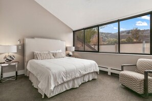A bedroom with a large bed, two bedside tables, a chair, and a window with a view of a mountainous landscape. - Park Ave 296 | Heated Pool | Hot Tub | Renovated | Stone Fireplace | Next to Golf Course | Free Bus (Park City)