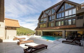 A two-story building with a swimming pool, outdoor seating, and a view of the mountains. - Resort Center 5000 | Ski-In/Ski-Out | Pool & Hot Tub Access | Steam Shower | Bunk Beds | Renovated (Park City)
