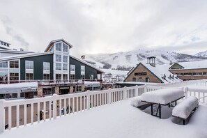 A snow-covered outdoor area with a white fence, benches, and buildings in the background. - Resort Center 5025 | Ski-In/Ski-Out | Pool & Hot Tub Access | Renovated Baths | Fireplace | Roku (Park City)