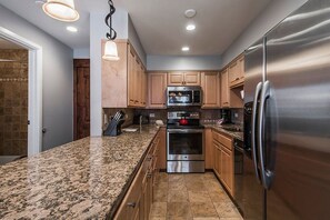A kitchen with granite countertops, stainless steel appliances, wooden cabinets, and pendant lighting. - Resort Center 5025 | Ski-In/Ski-Out | Pool & Hot Tub Access | Renovated Baths | Fireplace | Roku (Park City)