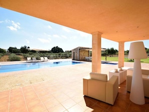 A covered outdoor area with a swimming pool, lounge chairs, and a table with a lamp. - Cabin in Muro With Swimming Pool (Muro)