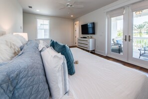 Ein Schlafzimmer mit einem großen Bett, einem Fernseher an der Wand und einer Glastür zu einem Außenbereich.