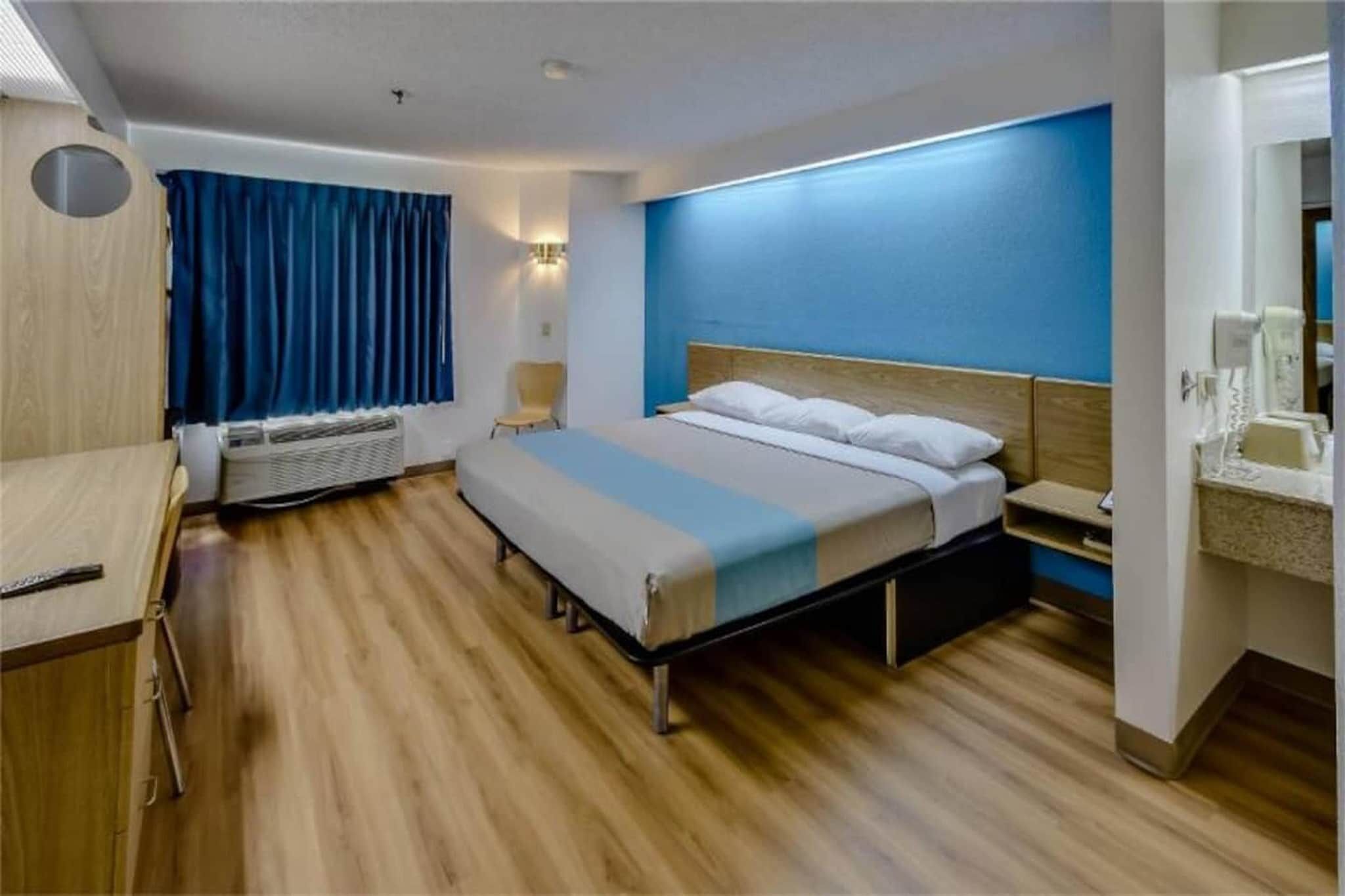 A hotel room with a bed, bedside table, and a desk with a chair.