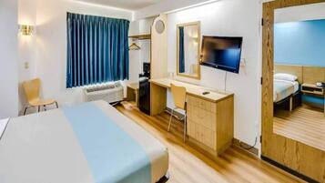 A hotel room with a bed, desk, chair, TV, and a wardrobe.