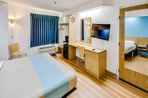 Una habitación de hotel con cama, escritorio, silla, televisor y armario.
