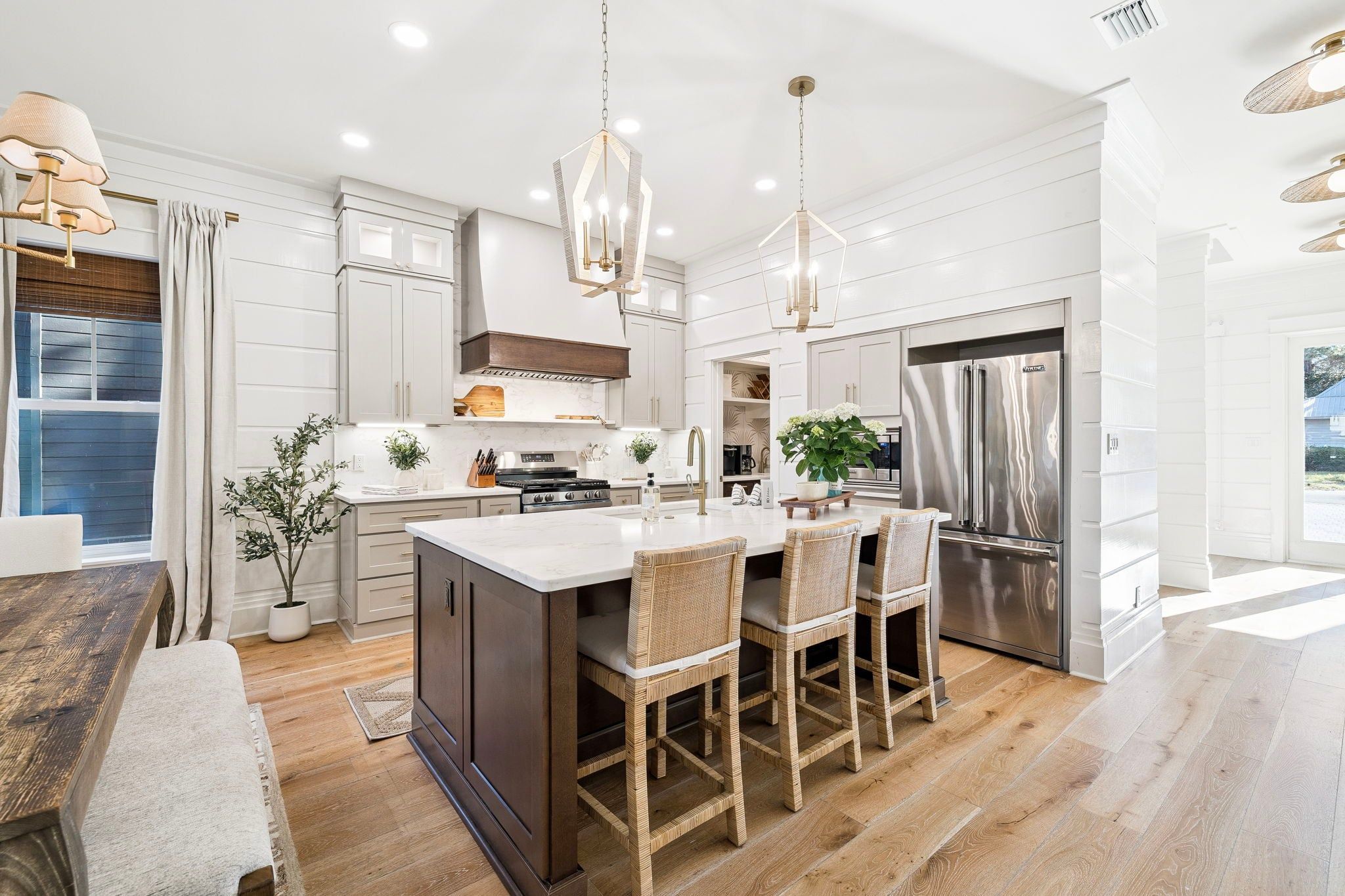 A modern kitchen with white cabinetry, a central island with bar stools, stainless steel appliances, and pendant lighting.