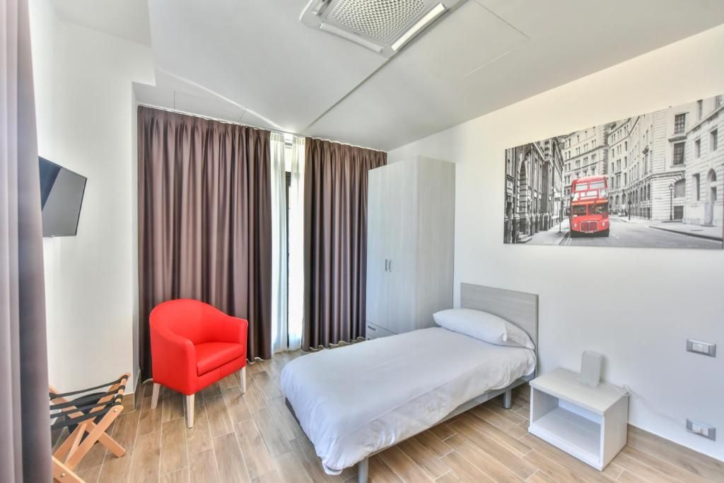 Una habitación de hotel moderna con una cama, un sillón rojo, un televisor y un cuadro de un paisaje urbano en la pared.