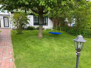 A well-maintained lawn with a swing set, a lamp post, and a white building with a door and windows. - Holiday Home With 1 Bedroom (Reinsbüttel)