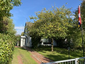 A white building with a sloped roof, a brick pathway leading to it, and a flagpole with a flag. - Holiday Home With 1 Bedroom (Reinsbüttel)