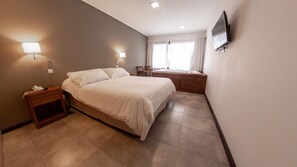 A hotel room with a bed, bedside lamps, a TV mounted on the wall, and a window with curtains. - Rincon del Duende (Mar de Las Pampas)