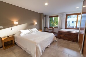 A bedroom with a bed, bedside tables, a chair, a window, and a wooden bench. - Rincon del Duende (Mar de Las Pampas)