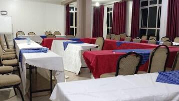 Ein Konferenzraum mit mehreren Tischen, Stühlen, einer Tafel und roten Vorhängen.